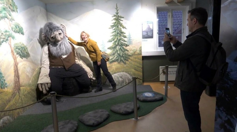 a man takes picture of a woman near a huge troll